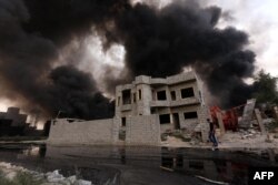 FILE - An Iraqi man walks near smoke billowing from oil wells, set ablaze by Islamic State group militants before fleeing the oil-producing region of Qayyarah, Aug. 30, 2016.