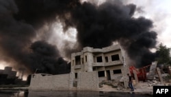 FILE - An Iraqi man walks near smoke billowing from oil wells, set ablaze by Islamic State (IS) group militants before fleeing the oil-producing region of Qayyarah, Aug. 30, 2016.