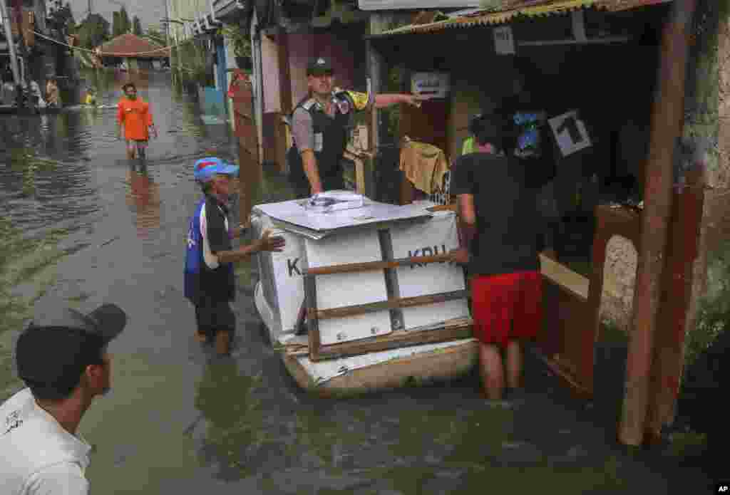 Para petugas pemilu membawa perlengkapan pemilu melewati jalan yang tergenang banjir di Bandung, Jawa Barat, 16 April 2019. (Foto: AP)