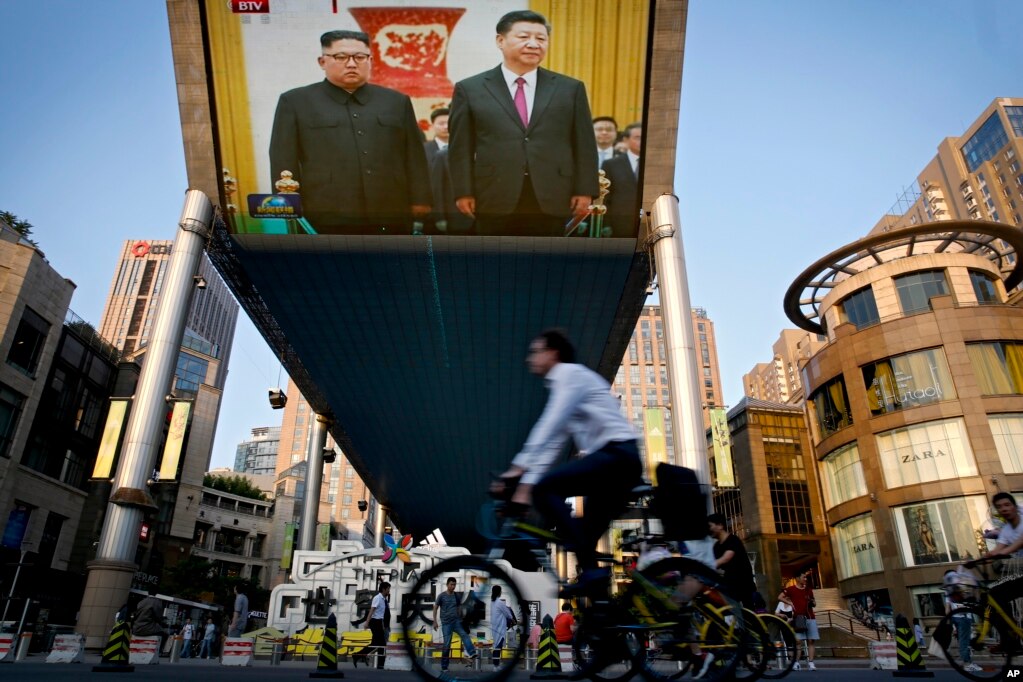 중국 베이징 거리에서 김정은 북한 국무위원장과 시진핑 중국 국가주석이 인민대회당에서 열린 환영식에 참석한 모습이 중계되는 대형 TV 화면 앞을 자전거를 탄 행인이 지나가고 있다.