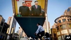 Les gens passent devant un écran de télévision géant retransmettant la réunion du dirigeant nord-coréen Kim Jong Un et du président chinois Xi Jinping lors d'une cérémonie de bienvenue au Grand Palais du Peuple à Beijing, mardi 19 juin 2018. 