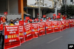 Người biểu tình với biểu ngữ ghi dòng chữ: "Chúng tôi, nhân dân Myanmar, hoàn toàn ủng hộ mọi hành động mà LHQ và Hoa Kỳ có thể đề ra chống "Độc tài Khủng bố" trong cuộc biểu tình chống đảo chính quân sự. Ảnh chụp trước Ngân hàng Kinh tế Myanmar ở Mandalay, Myanmar, ngày 15/2/2021. AP