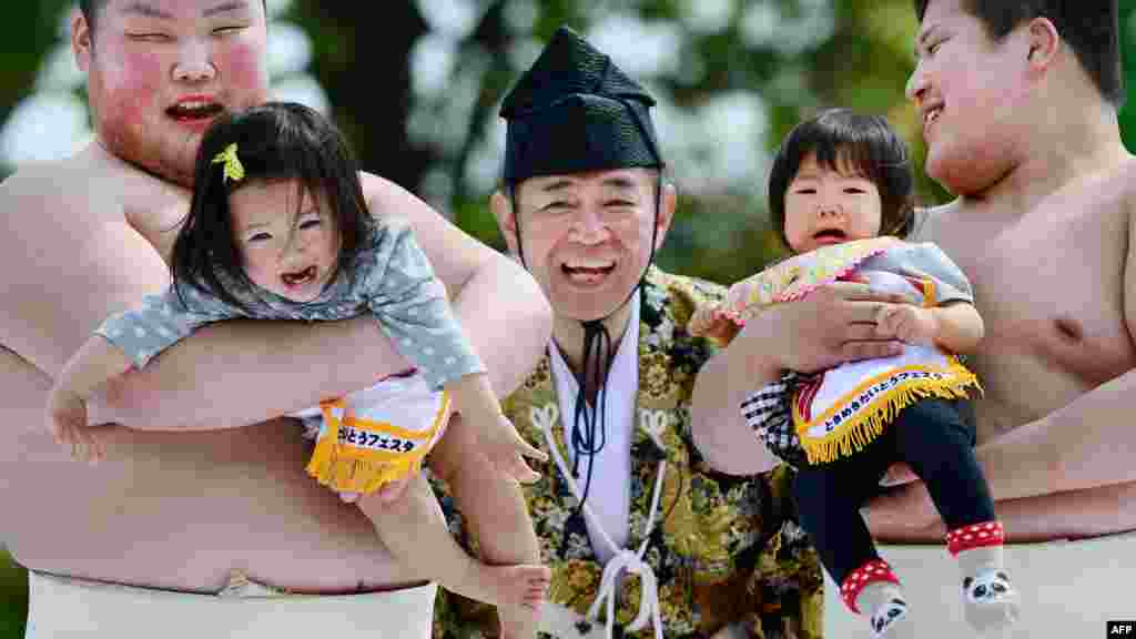 Débés portés par deux étundiants lutteurs de sumo pleurent à côté d&#39;un arbitre (C) vêtu d&#39;un costume traditionnel lors de la compétition &quot;Baby-cry Sumo&quot; au temple Sensoji à Tokyo le 29 Avril 2013.