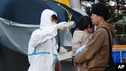 A man and his child who have just arrived from inside the danger zone in Fukushima Prefecture are checked for abnormal radiation levels, Sunday, 13 March 2011