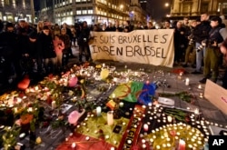 People holding a banner reading "I am Brussels" behind flowers and candles to mourn for the victims at Place de la Bourse in the center of Brussels, March 22, 2016.