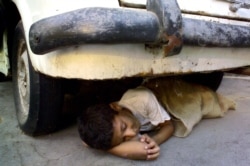 Seorang anak tunawisma Mesir tidur di bawah sebuah mobil tua berkarat di sebuah jalan di Kairo, 20 Agustus 2004. (Foto: Reuters)