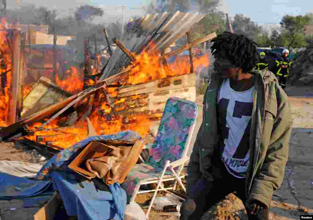 Seorang migran melewati tempat penampungan yang dibakar dalam protes melawan pembongkaran kamp migran di Calais, pada hari kedua evakuasi dan pemindahan mereka (25/10). (Reuters/Pascal Rossignol)