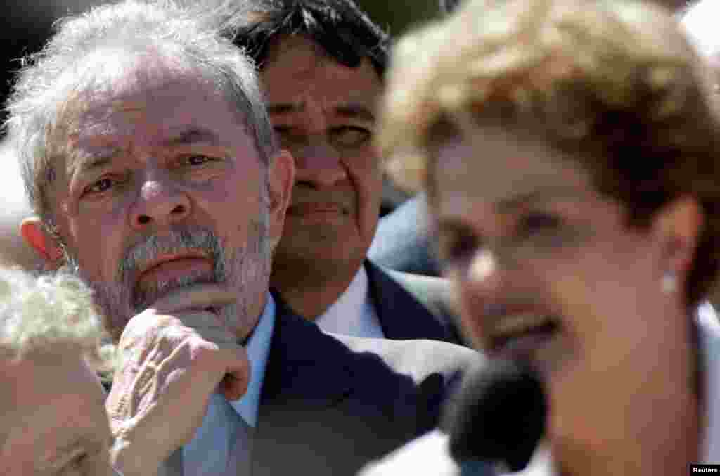 Em destaque na foto a face de Lula da Silva, ex-Presidente do Brasil, ouvindo Dilma Rousseff à saída do Palácio do Planalto, endereçando um discurso aos seus apoiantes