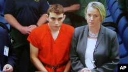 A video monitor shows school shooting suspect Nikolas Cruz, left, making an appearance before Judge Kim Theresa Mollica in Broward County Court, Feb. 15, 2018, in Fort Lauderdale, Florida. Cruz is accused of opening fire Wednesday at the school killing more than a dozen people and injuring several. 