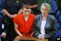 A video monitor shows school shooting suspect Nikolas Cruz, left, making an appearance before Judge Kim Theresa Mollica in Broward County Court, Feb. 15, 2018, in Fort Lauderdale, Florida.