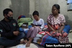 Murid kelas V SD Qayran Ruby Al Maghribi, tengah didampingi orang tuanya Fahroji, kiri, dan Yulia, memeriksa ponsel bekas yang dikirimkan oleh Ghina Ghaliya. (Foto: AP / Tatan Syuflana)