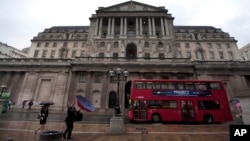 FILE - People hold umbrellas to shelter from the rain as they walk past the Bank of England in London, Aug. 4, 2011. The IMF has said that Britain's vote to leave EU has created a "sizeable increase in uncertainty."