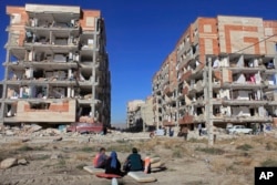 Survivors sit in front of buildings damaged by an earthquake, in Sarpol-e-Zahab, western Iran, Nov. 13, 2017.