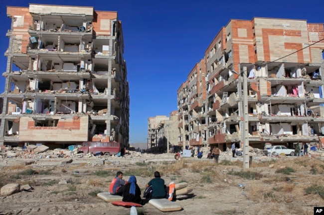 Survivors sit in front of buildings damaged by an earthquake, in Sarpol-e-Zahab, western Iran, Nov. 13, 2017.