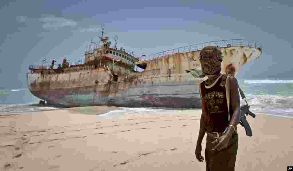 A masked Somali pirate stands near a Taiwanese fishing vessel that washed up on shore after the pirates were paid a ransom and released the crew, in the once-bustling pirate den of Hobyo, Somalia, Sept. 23, 2012. 