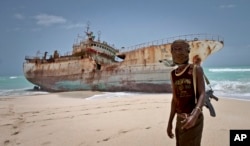 FILE - A masked Somali pirate stands near a fishing vessel that washed up on shore after the pirates were paid a ransom and released the crew, in Hobyo, Somalia, Sept. 23, 2012.