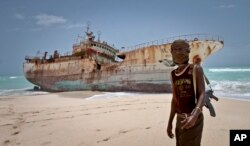 FILE - A masked Somali pirate stands near a Taiwanese fishing vessel that washed up on shore after the pirates were paid a ransom and released the crew, in the once-bustling pirate den of Hobyo, Somalia, Sept. 23, 2012.