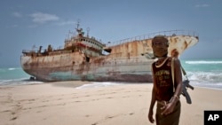 FILE - A masked Somali pirate stands near a Taiwanese fishing vessel that washed up on shore after the pirates were paid a ransom and released the crew, in Hobyo, Somalia, September 2012.