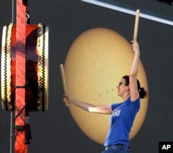 A large screen with a live telescope feed of the sun is visible behind Karen Tingey as she drums with Portland Taiko during a rehearsal in preparation for Monday's solar eclipse, in Salem, Ore.