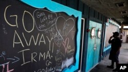 FILE - A chalkboard is decorated with messages regarding the approaching Hurricane Irma as a person reads a sign stating a restaurant is closed in Flagler Beach, Fla., Sept. 8, 2017. 
