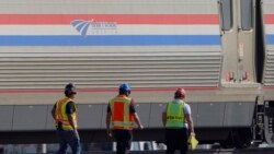 Workers walk past a baggage car, Sept. 27, 2021, from an Amtrak train that derailed Saturday, near Joplin, Mont.