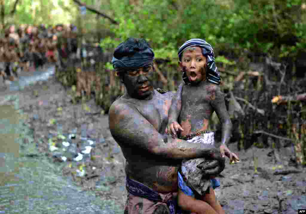 Seorang pria Bali menggendong anak laki-lakinya pada tradisi mandi lumpur atau &quot;Mabuug-buugan&quot; di desa Kedonganan, dekat Denpasar.