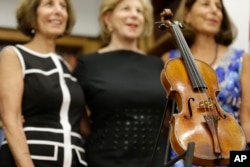 Sisters Jill Totenberg, left, Nina Totenberg, center, and Amy Totenberg pose for pictures with the recovered Ames Stradivarius violin during a news conference in New York, Aug. 6, 2015.