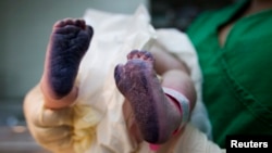 Một em bé vừa mới sinh trong một bệnh viện phụ sản ở Caracas, Venezuela, với đôi bàn chân được in trong mực để làm giấy khai sinh