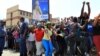 FILE - Police officers watch as crowds of people gather outside a police station in the Diepsloot area, north of Johannesburg, South Africa.