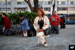 People kneel during a Mass held outside the Parish of Santiago Apostol, where church officials were waiting for inspectors to check damages following the recent earthquake, in the Plaza de las Tres Culturas in Tlatelolco, Mexico City, Sept. 24, 2017.