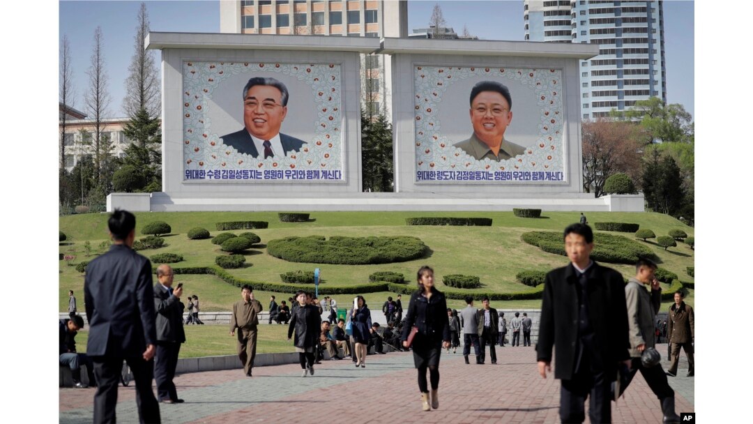 FILE - People walk beneath portraits of late leaders, Kim Il Sung, left, and Kim Jong Il, in Pyongyang, North Korea, April 18, 2017.