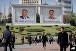 people walk beneath portraits of late leaders, Kim Il Sung, left, and Kim Jong Il, in Pyongyang, North Korea, April 18, 2017.