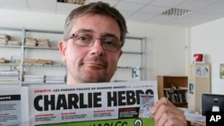 FILE - Publishing director of the satiric weekly Charlie Hebdo, "Charb," displays the front page of the newspaper, in Paris, Sept. 19, 2012. 