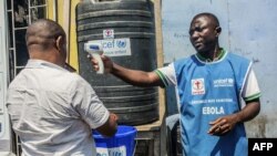 Un homme se lave les mains au chlore alors qu'un agent de santé vérifie sa température à Goma en RDC le 15 juillet 2019.