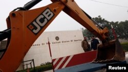 Policemen stand next to a bulldozer removing the security barriers in front of the U.S. embassy in New Delhi on December 17, 2013. 