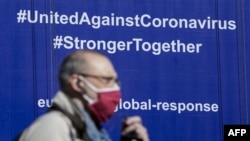 布魯塞爾一名戴著口罩的行人從歐盟委員會大樓掛有“全球應對新冠病毒”字樣的標語前走過。（2020年5月6日）