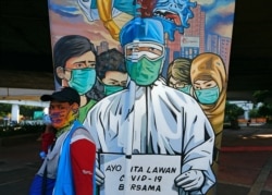 Seorang pedagang yang mengenakan masker pelindung berjalan melewati mural yang mempromosikan kesadaran akan wabah Covid-19 di Jakarta, 1 Desember 2020. (Foto: REUTERS/Ajeng Dinar Ulfiana)