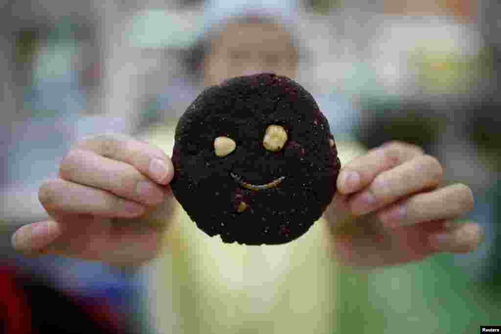 A sales assistant poses for photographs with a mealworm cookie in Seoul, South Korea.