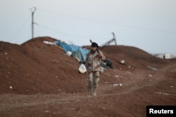 A rebel fighter from Jaysh al-Sunna carries food as he walks along a sand barricade in Tel Mamo village, in the southern countryside of Aleppo, Syria, March 13, 2016.