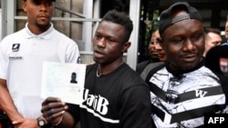 Malian migrant Mamoudou Gassama, center, with his older brother at right, holds his temporary residence permit after receiving it at the Prefecture of Bobigny, northeast of Paris, May 29, 2018. 