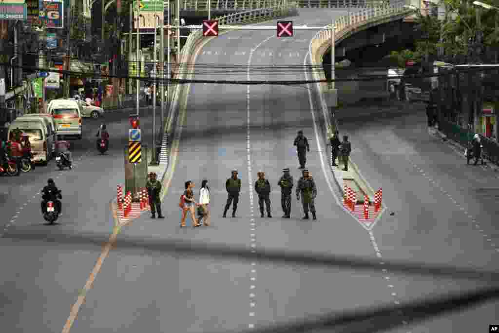 People make their way past a line of Thai soldiers guarding the street near Victory Monument to prevent anti-coup demonstrations in Bangkok, May 30, 2014.