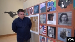 Artist Ric Garcia stands in front of a wall of panels, each one representing the immigrant background of a different artist. Garcia's is the panel from Cuba. (Jsoh/VOA)