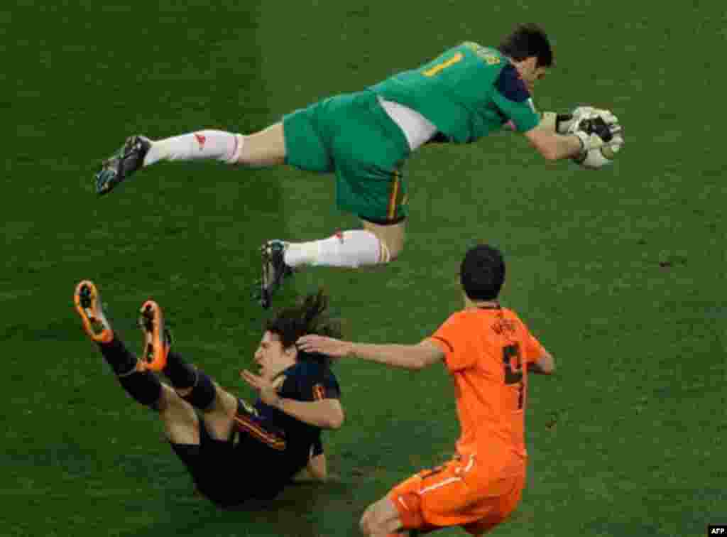 Spain goalkeeper Iker Casillas, top, makes a save over Netherlands' Robin van Persie, right, and Spain's Carles Puyol during the World Cup final soccer match between the Netherlands and Spain at Soccer City in Johannesburg, South Africa, Sunday, July 11, 