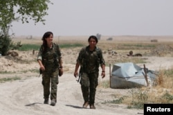 FILE - Kurdish female fighters from the People's Protection Units (YPG), operating alongside with the Syria Democratic Forces, walk in northern province of Raqqa, Syria, May 27, 2016.