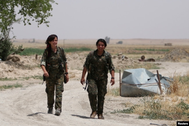 FILE - Kurdish female fighters from the People's Protection Units (YPG), operating alongside with the Syria Democratic Forces, walk in northern province of Raqqa, Syria, May 27, 2016.