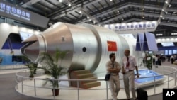 FILE - Visitors sit besides a model of China's Tiangong 1 space station at the 8th China International Aviation and Aerospace Exhibition in Zhuhai city, south China, in November 2010. Tiangong 2 will be sent into space Thursday.