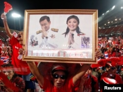A red-shirted supporter holds up a pictures of Thailand's Prime Minister Yingluck Shinawatra and her brother Thaksin Shinawatra, during a rally at Rajamangala national stadium in Bangkok, Nov. 19, 2013.