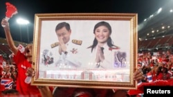 A red-shirted supporter holds up a pictures of Thailand's Prime Minister Yingluck Shinawatra and her brother Thaksin Shinawatra, during a rally at Rajamangala national stadium in Bangkok, Nov. 19, 2013.