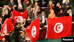 Members of the Tunisian parliament wave flags after approving the country's new constitution in the assembly building in Tunis, Jan. 26, 2014.