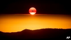 FILE - A plane battling the Ferguson Fire passes the setting sun over unincorporated Mariposa County, Calif., near Yosemite National Park, July 15, 2018. 